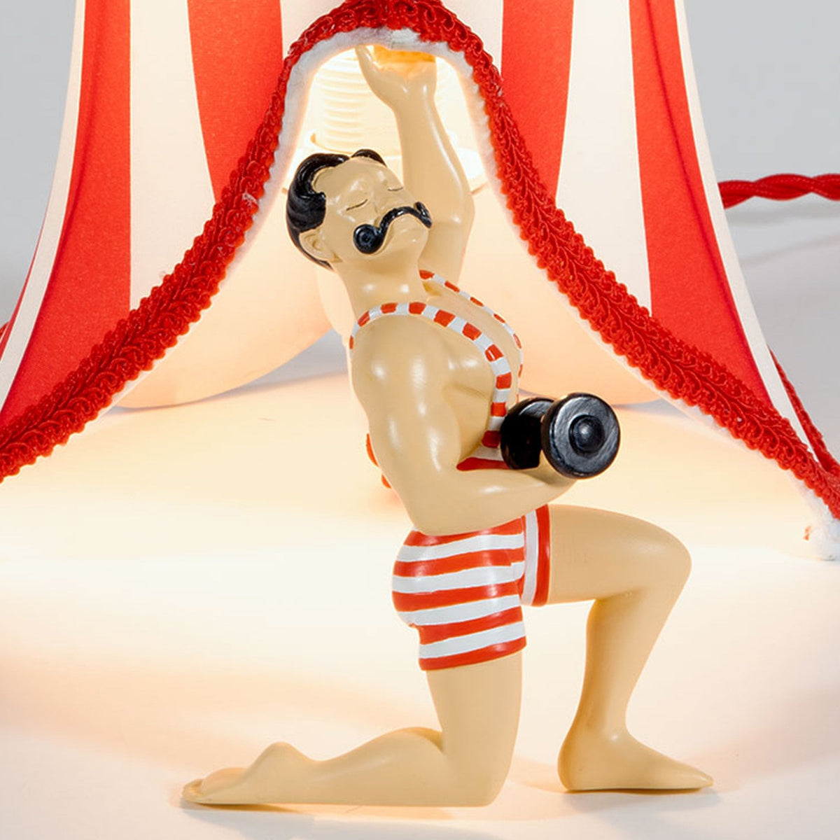 Close-up of the circus strongman's face, torso, and arm, holding the lampshade.