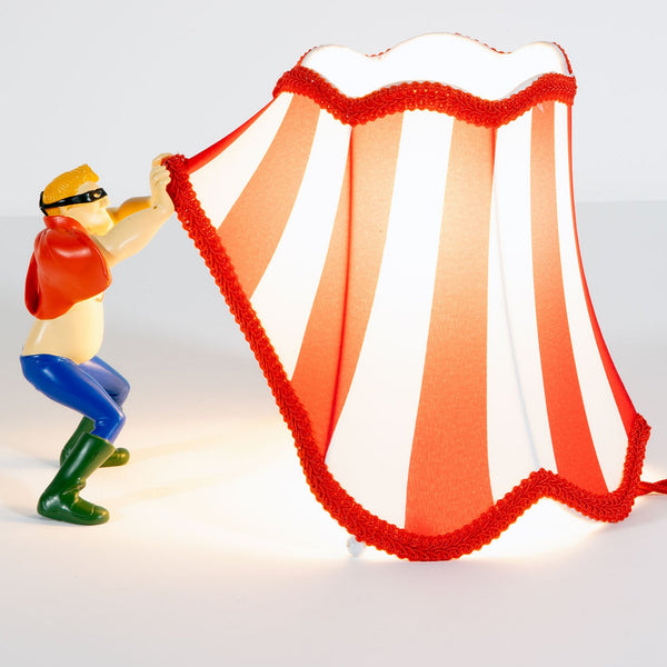 A figurine holding up a red and white striped lampshade with red trim, resembling a circus tent.