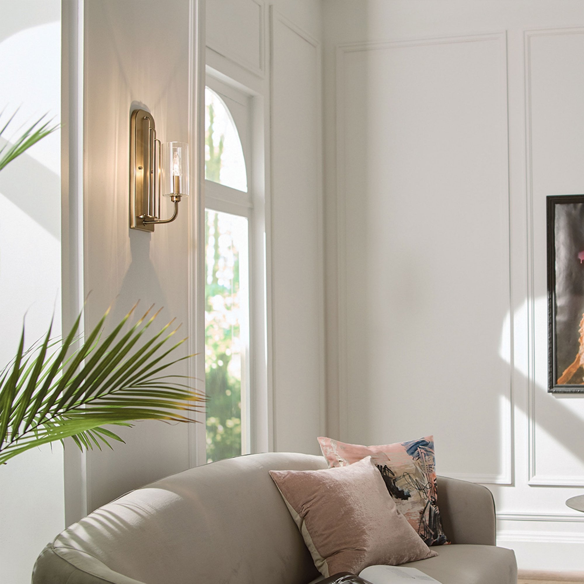 A modern living room with a brass wall light illuminating a neutral sofa.