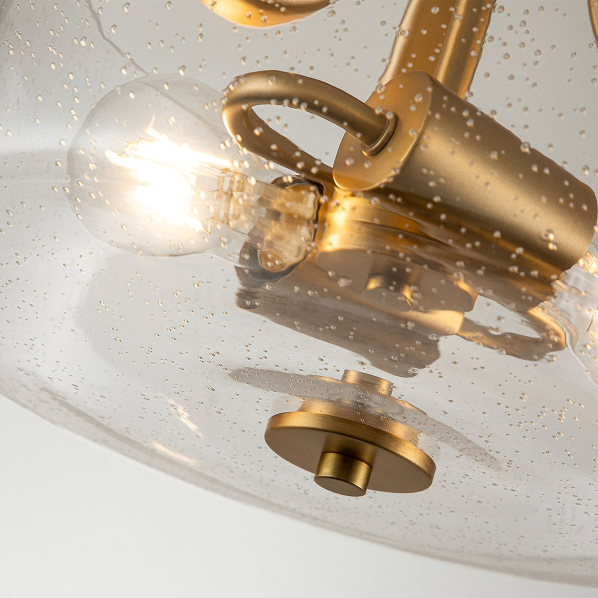 A close-up of the seeded glass shade and bulb fittings of a brass ceiling light.