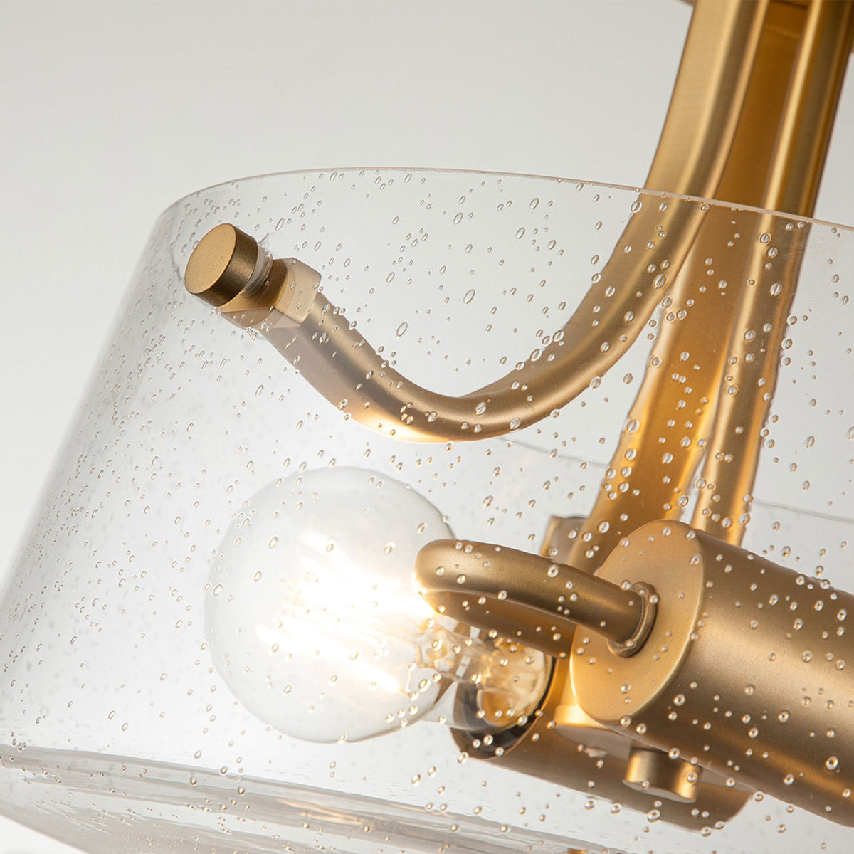A close-up of the seeded glass shade, brass arms, and light bulb of the ceiling fixture.