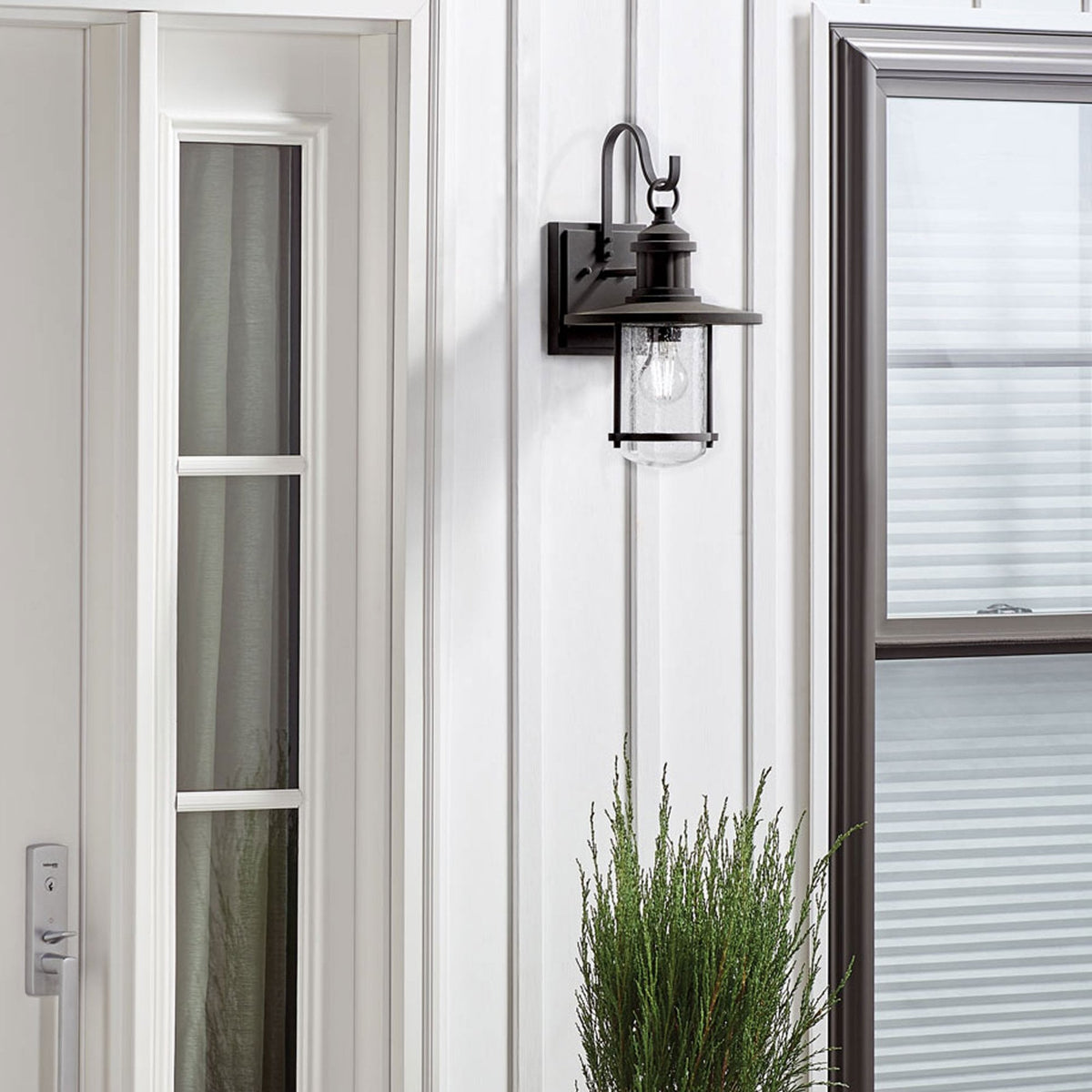 A black outdoor wall light with a clear seeded glass shade illuminates a white exterior wall.