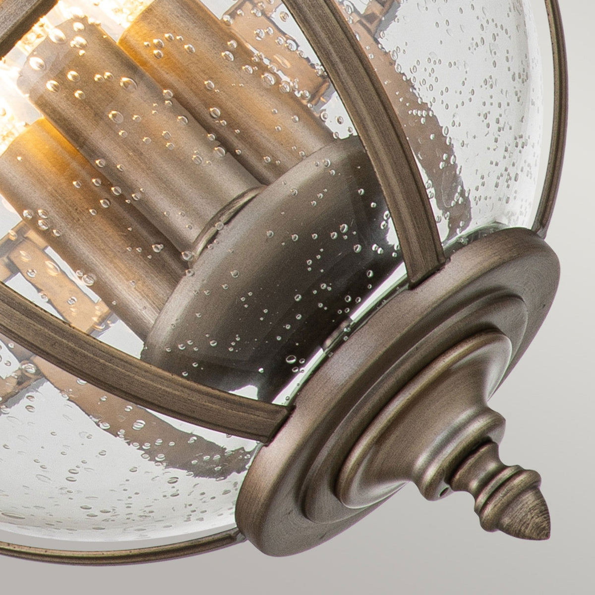 Close-up of the bottom finial and seeded glass of the bronze outdoor pendant light.