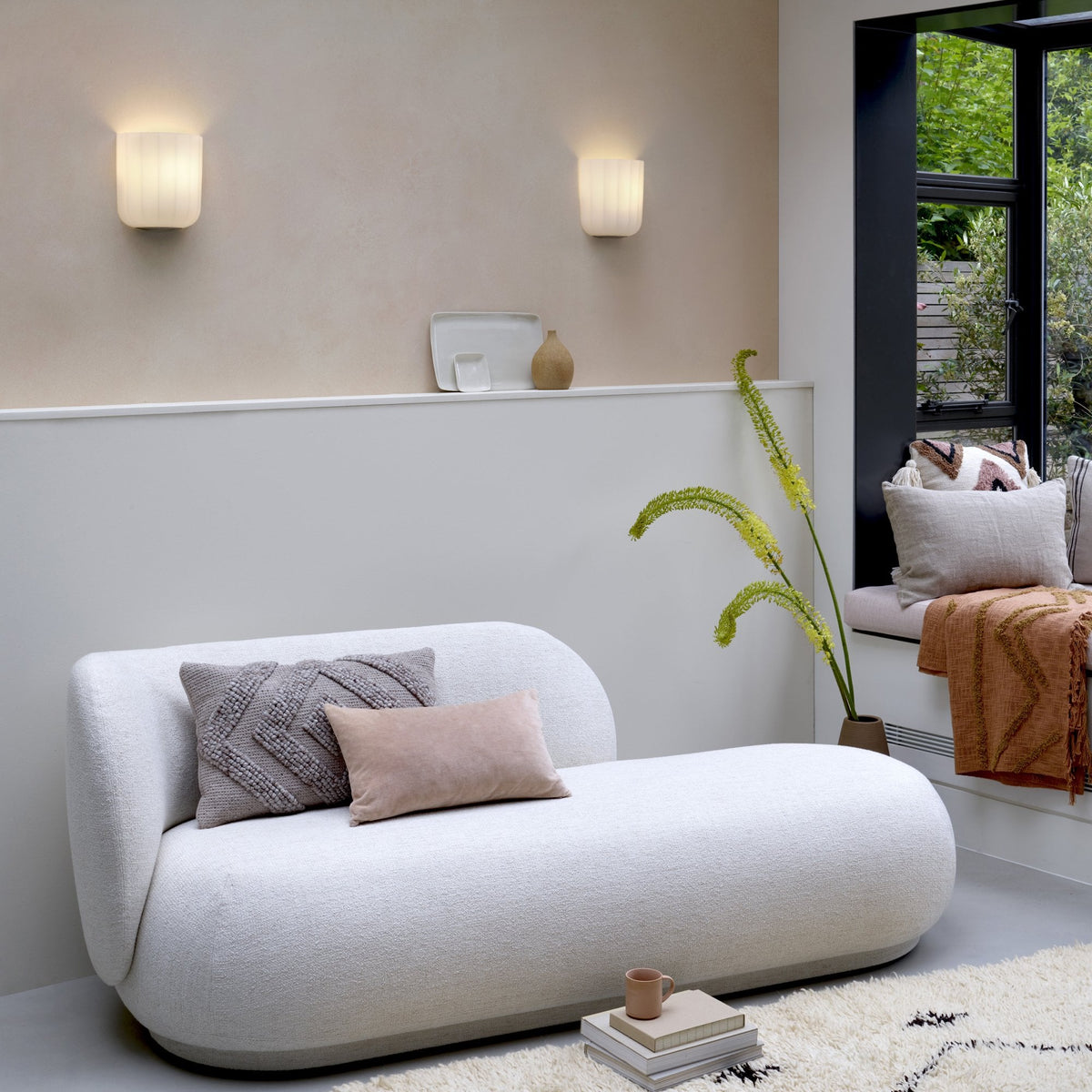 White chaise lounge with pillows, wall sconces, and a window seat with cushions and a throw