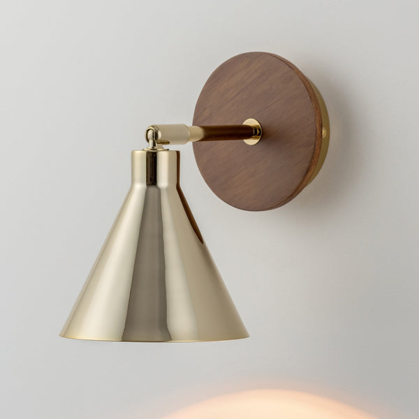 A modern wall lamp with a brass shade and wooden base, casting light downwards.
