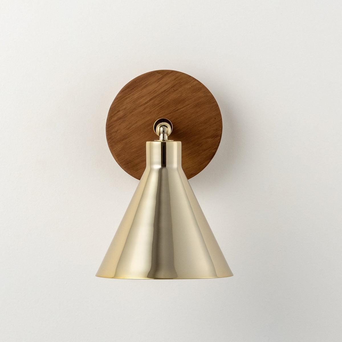 A modern wall lamp with a brass conical shade and a round wooden base.