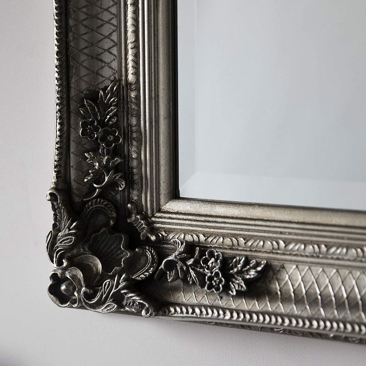 A close-up of the ornate silver frame of a mirror, showing floral and textured details.