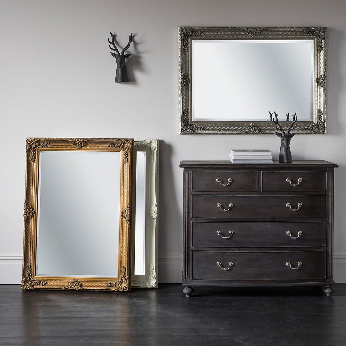 Three ornate mirrors: one gold, one white, and one silver hanging above a chest of drawers.