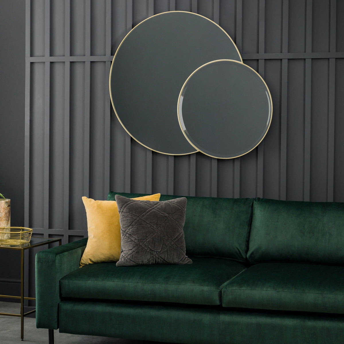 Two round gold-rimmed mirrors hang above a green velvet sofa with yellow and grey cushions.