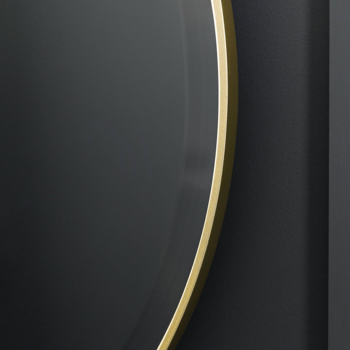 Close-up of the sleek gold frame of a round mirror against a dark background.