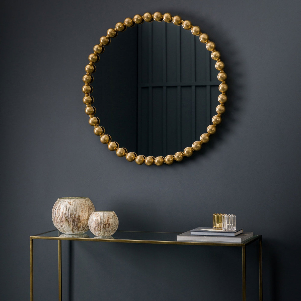 A round mirror with a gold beaded frame hangs above a gold console table.