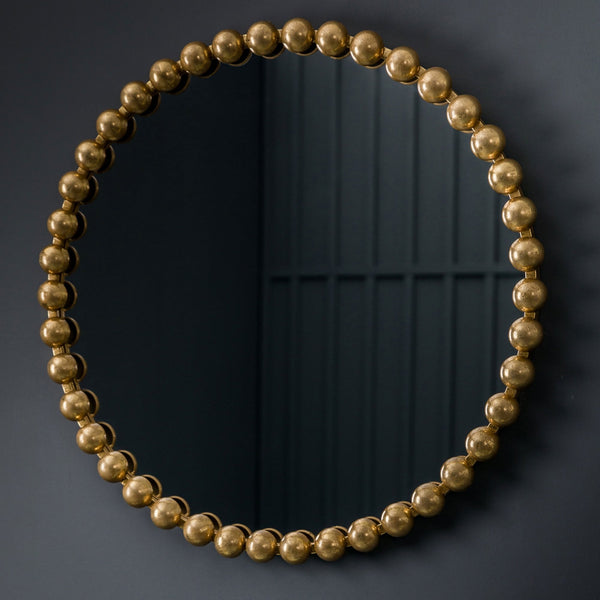 A close-up of a round mirror with a gold beaded frame.