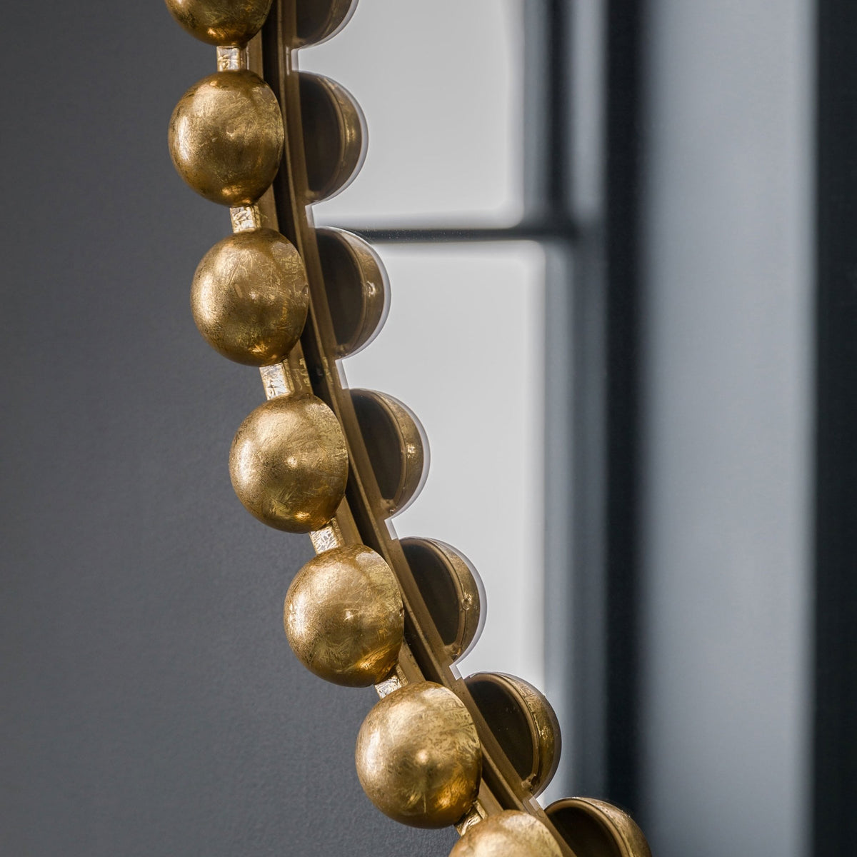 A side view of the gold beaded frame of a mirror reflecting a window.