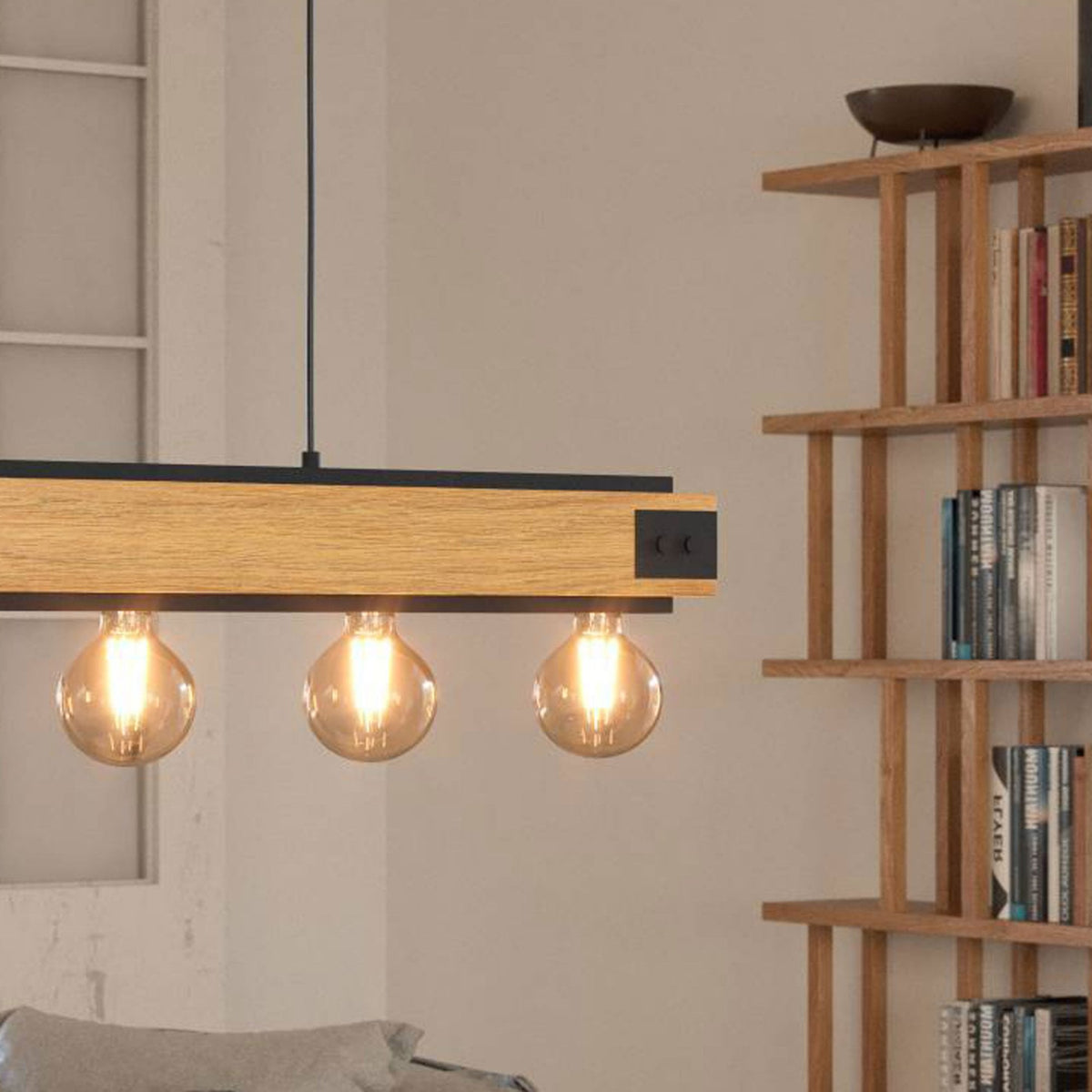 A wooden and metal light fixture with three exposed bulbs, illuminating a living room setting.