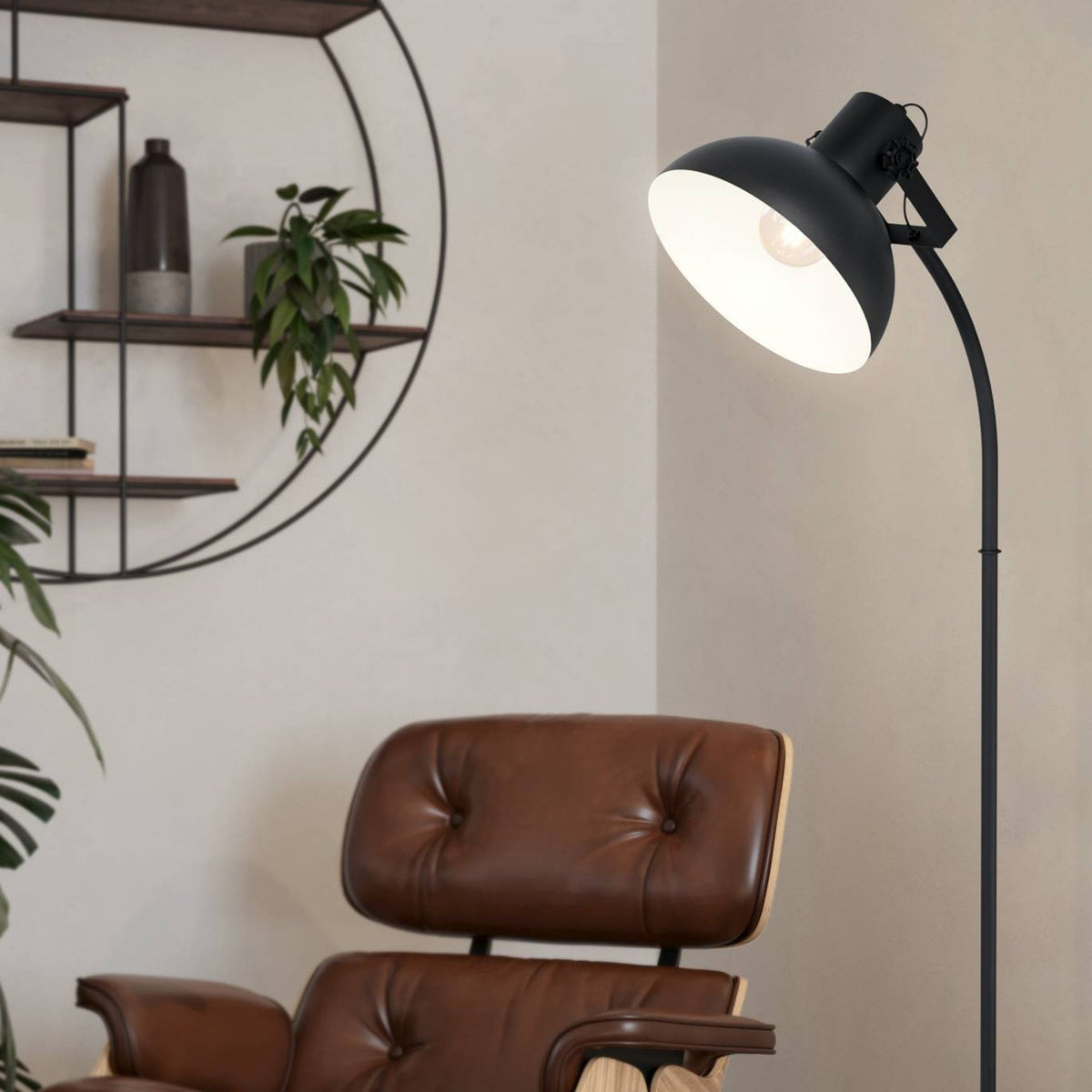 A black floor lamp next to a brown leather armchair and a circular wall shelf.