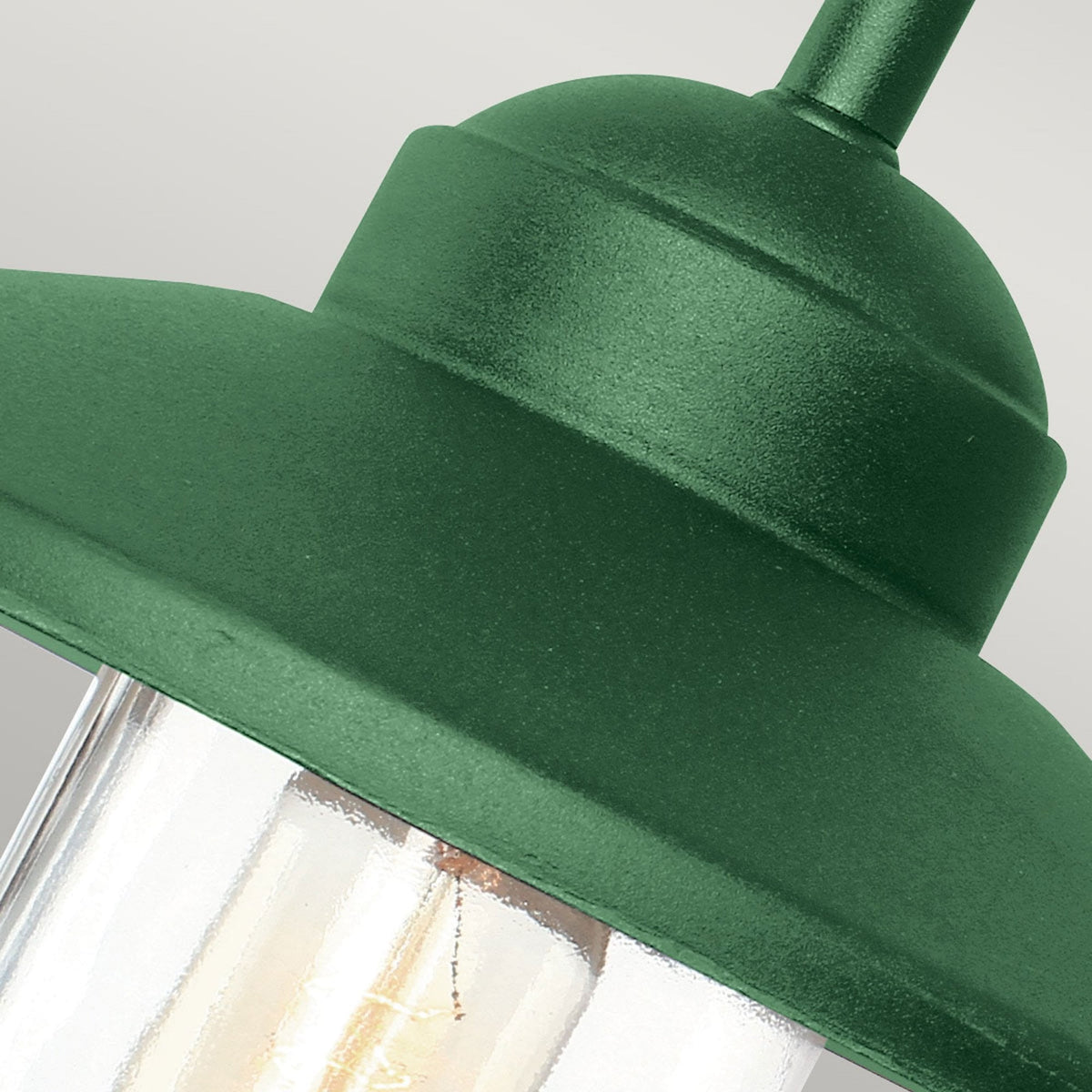 Close-up of the dark green metal shade and clear glass housing of a barn light.