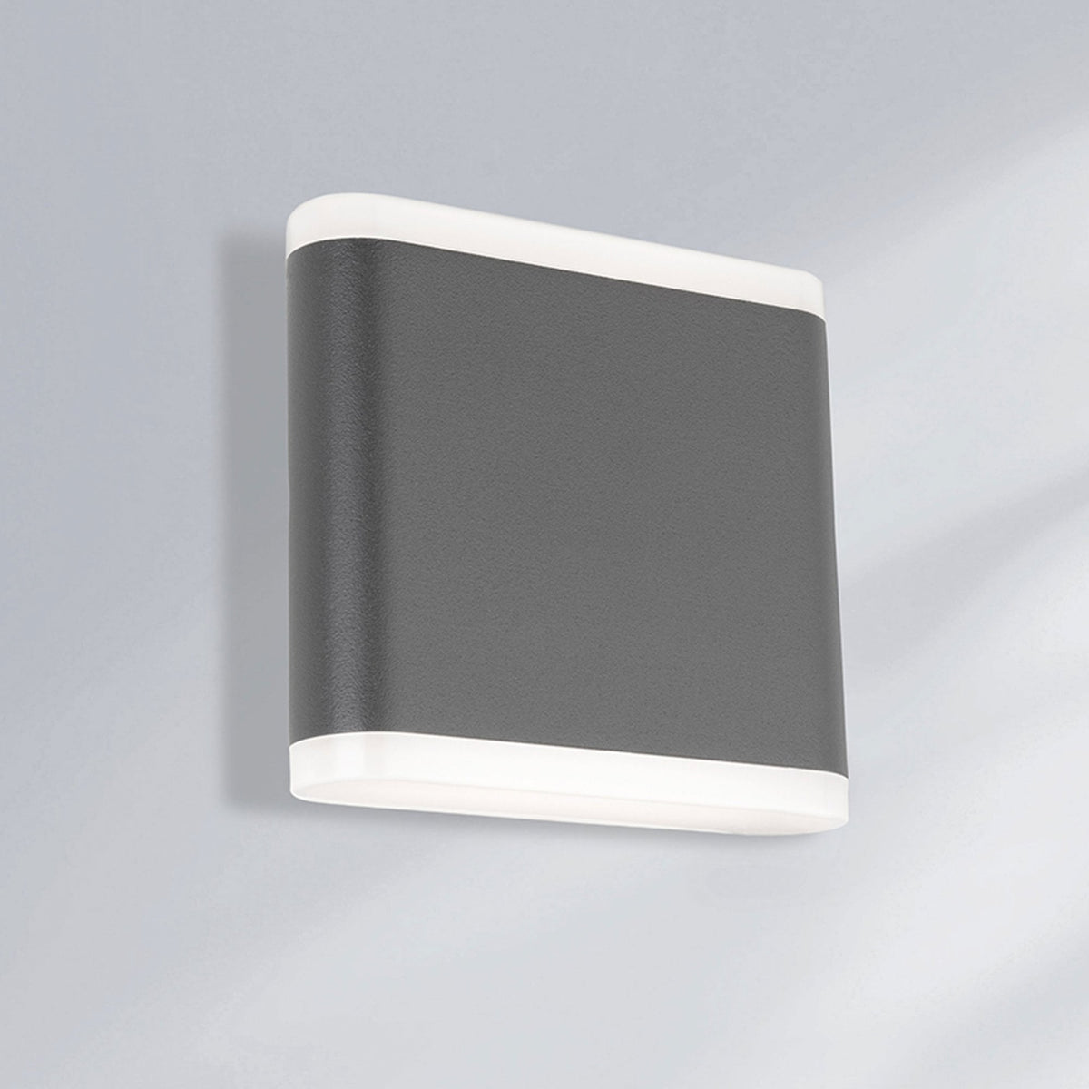 A modern grey and white rectangular wall light casts light upwards and downwards on a grey wall.