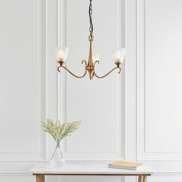 A three-light brass chandelier with frosted glass shades hangs above a white console table.