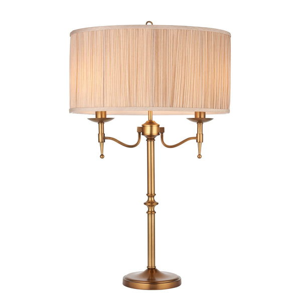 A sophisticated brass table lamp with a pleated shade and two candle-like fixtures.