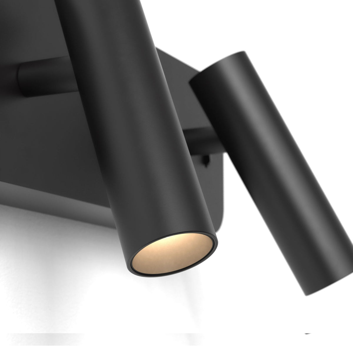 Two black cylindrical wall lights, one illuminated with a warm glow, mounted on a white wall