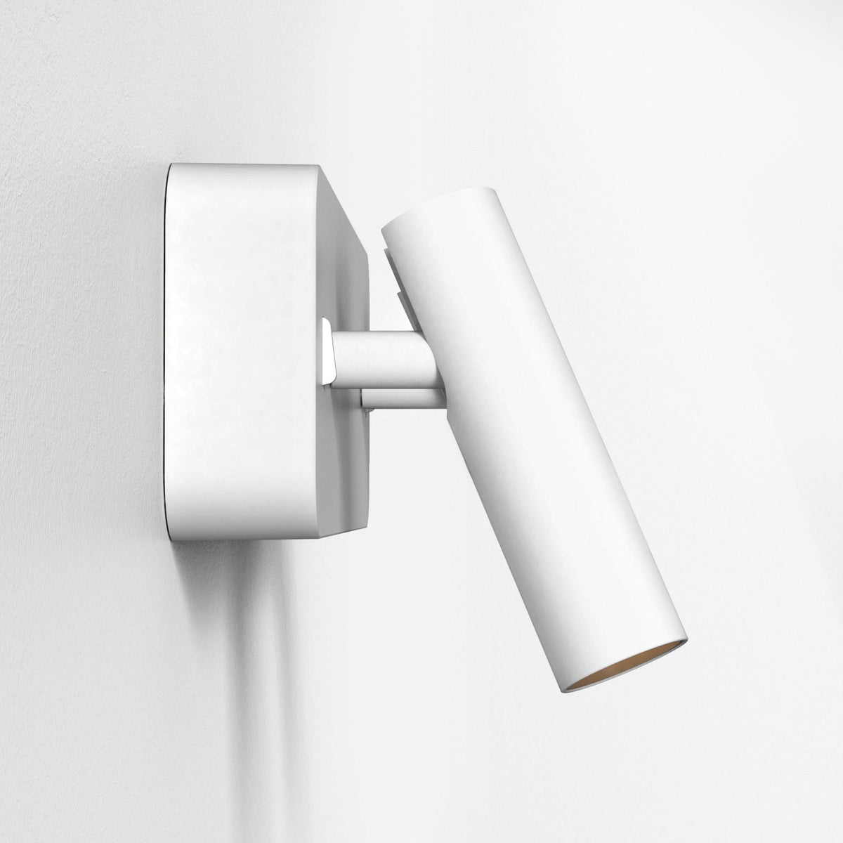 White wall mounted spotlight with a cylindrical head angled downwards, against a white textured wall