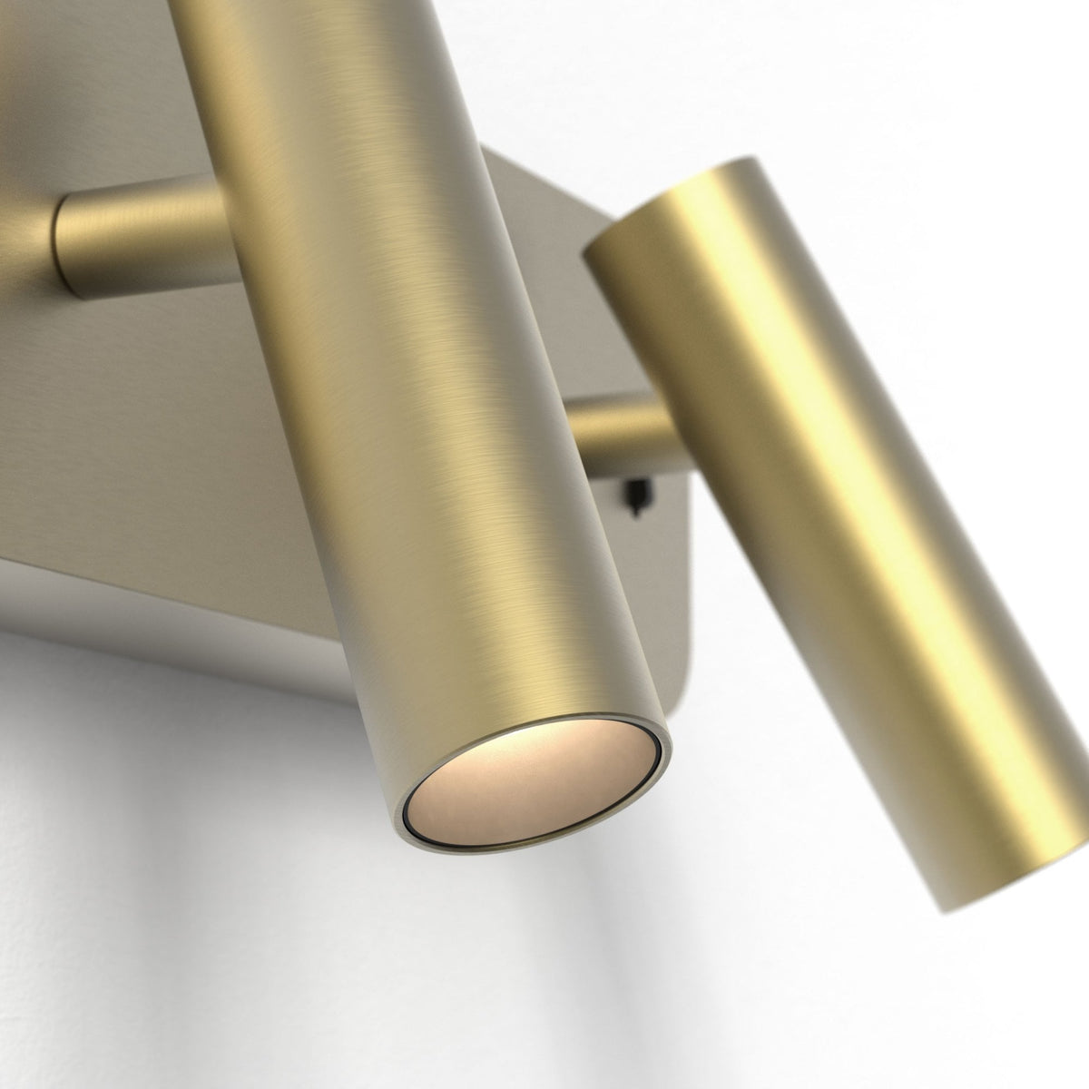 Two brass wall-mounted cylindrical lights, one illuminated, on a white wall