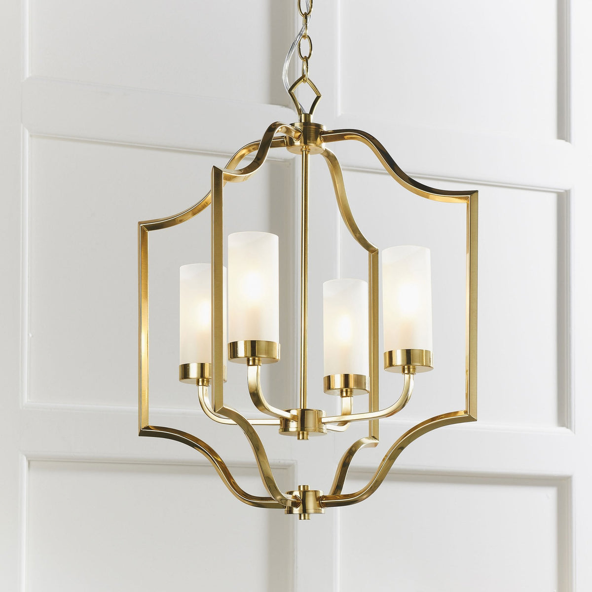 A gold chandelier with four frosted glass shades hangs against a white paneled wall.