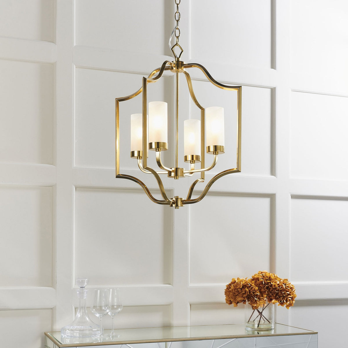 A gold chandelier with four frosted glass shades hangs above a console table with flowers and glasses.