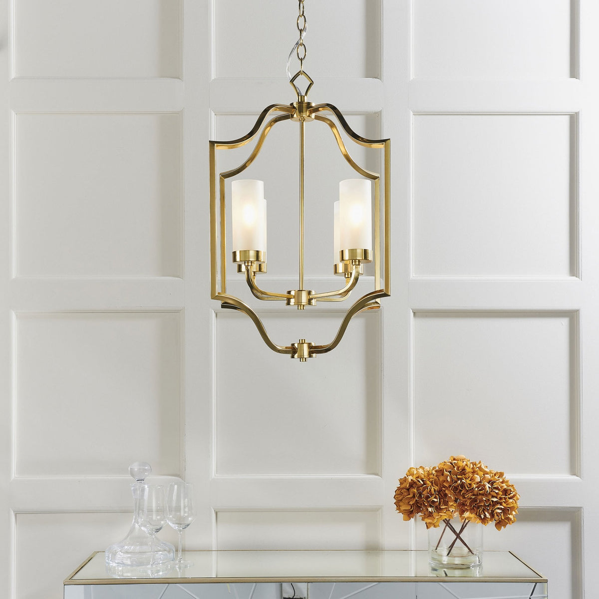 A gold chandelier with two frosted glass shades hangs above a console table with flowers and a decanter.