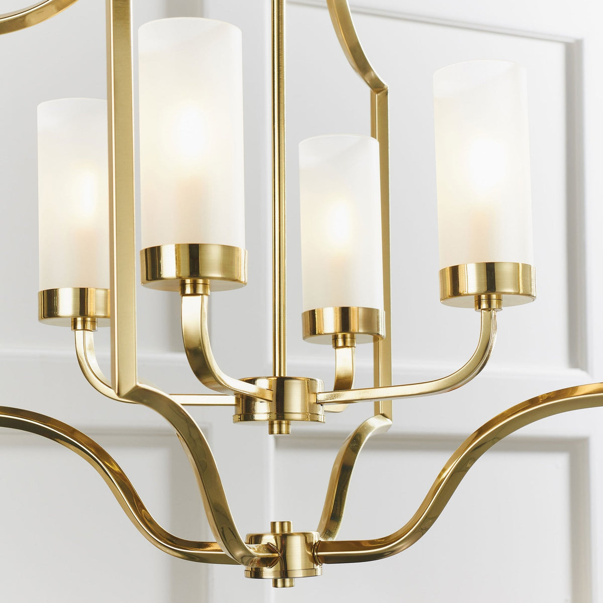 Close-up of a gold chandelier showing four frosted glass shades and intricate metalwork.