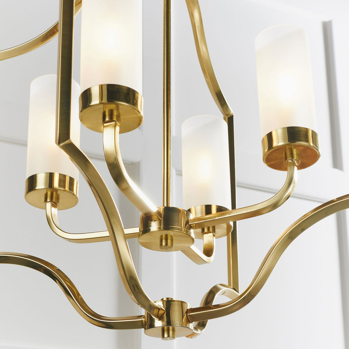 Close-up of a gold chandelier showing four frosted glass shades and detailed metal curves.