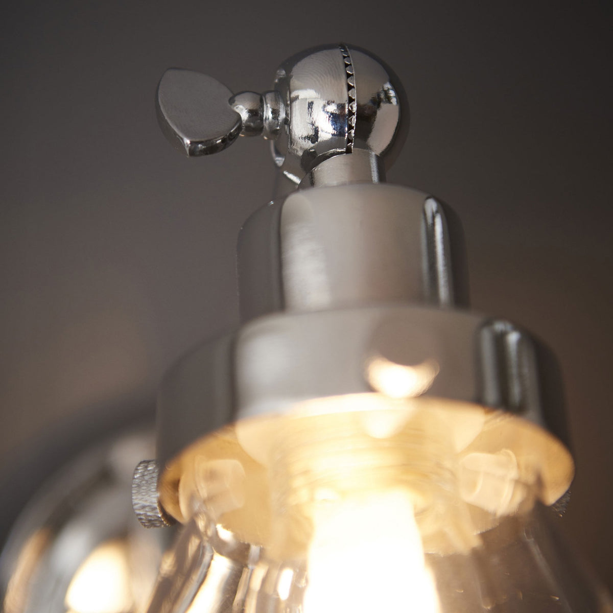 Detailed view of the polished chrome adjustable joint and top of the clear glass shade of a wall light.
