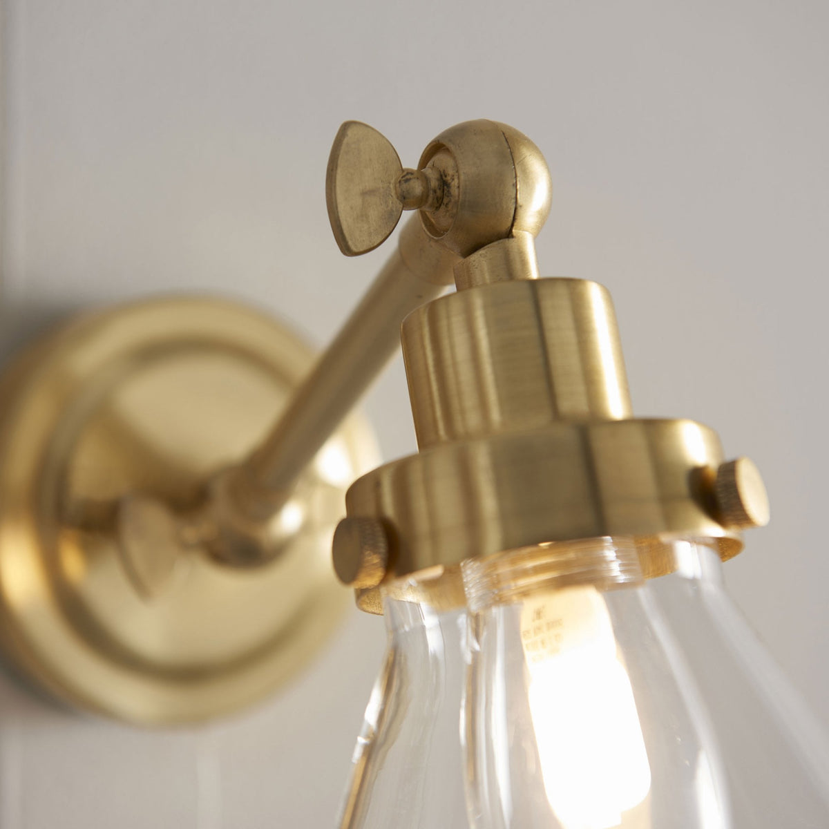 Close-up of the brass arm and clear glass cone shade of a wall light.