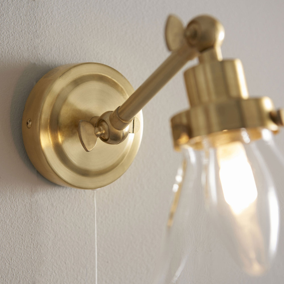 Close-up of the brass base and adjustable arm of a wall light with a clear glass shade.