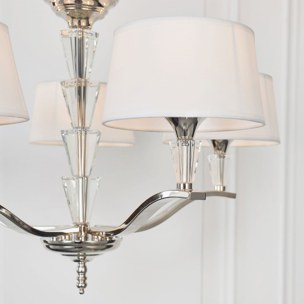 Close-up of a chandelier arm with a white fabric shade and clear crystal detail against a white wall.