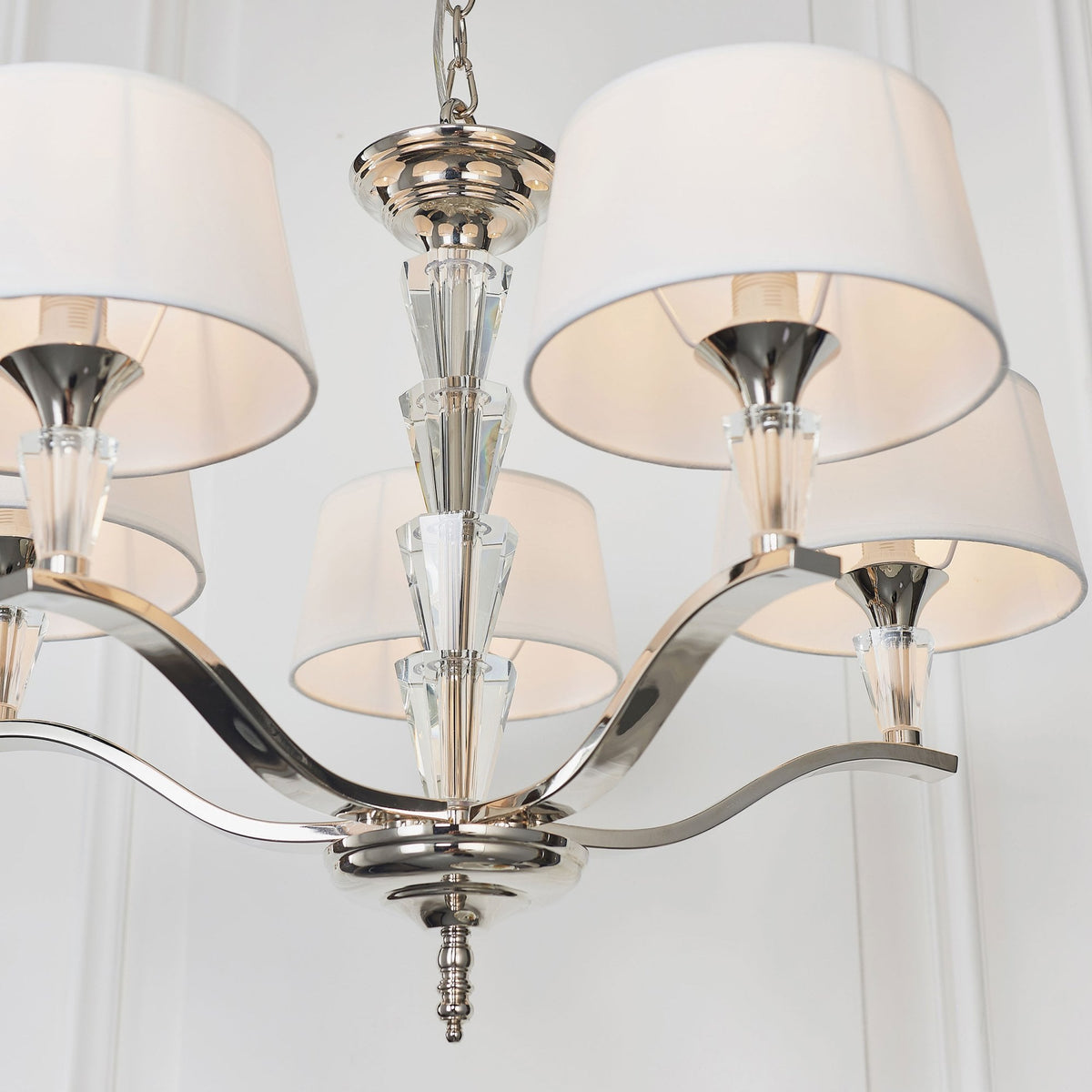Close-up of the central column and arms of a chandelier with white fabric shades and crystal details.