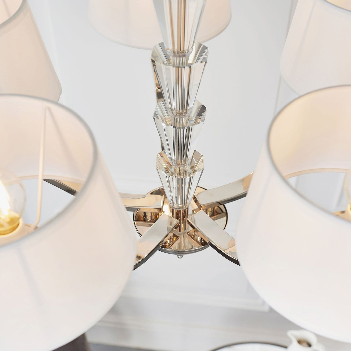 Overhead view of a chandelier showing the central crystal column and white fabric shades.