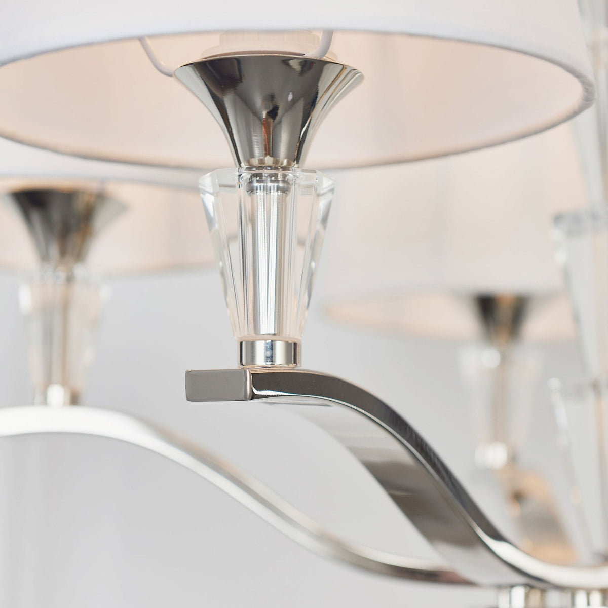 Detailed view of a chandelier arm with a white fabric shade, crystal accent, and polished metal finish.