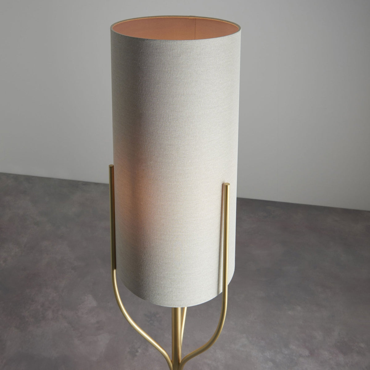 Close-up of the top of a floor lamp, showing the light-colored cylindrical shade and gold frame.