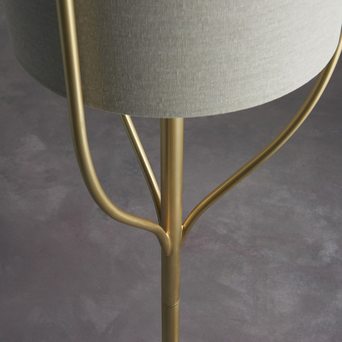Close-up of the gold base and support structure of a floor lamp with a light-colored shade.