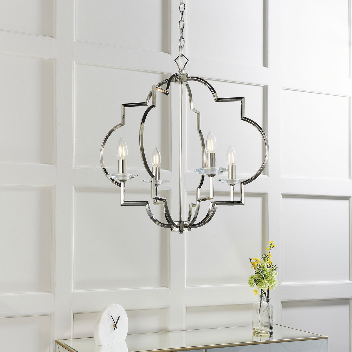 Polished nickel chandelier with four lights, geometric frame, and clear glass accents, hanging in a room with white paneled walls.