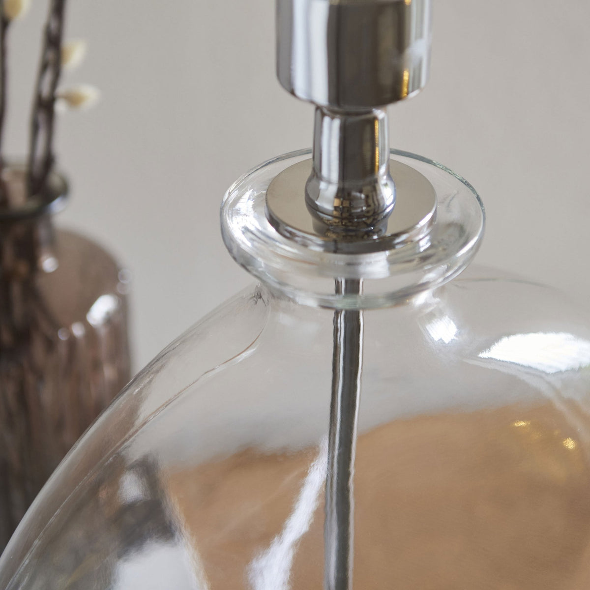 Close-up of the top of a clear glass lamp base, showing the metallic fitting and a hint of a white shade.