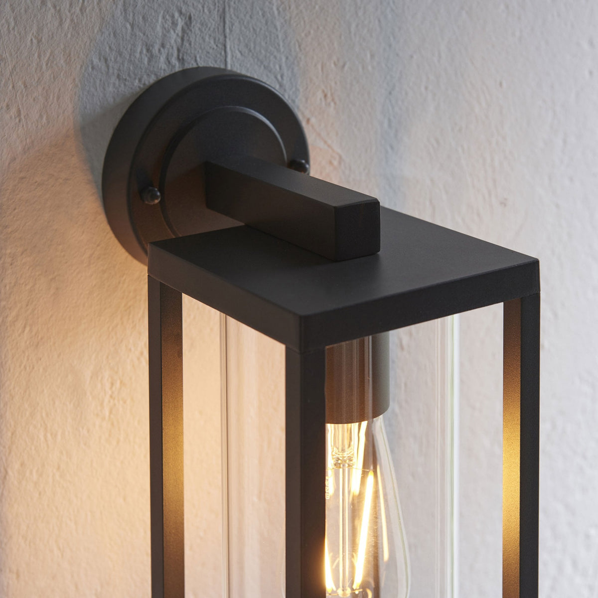 Top view of a black outdoor wall light with clear glass panels and an exposed filament bulb.
