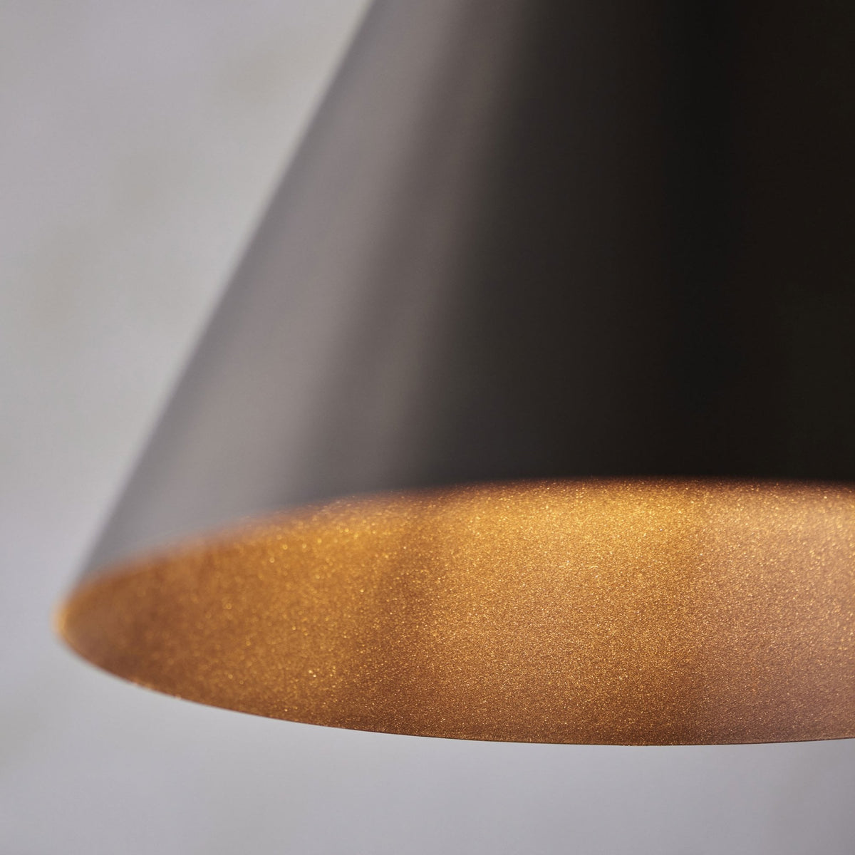 Close-up of the bottom edge of a dark bronze conical pendant light, showing a warm, textured interior.