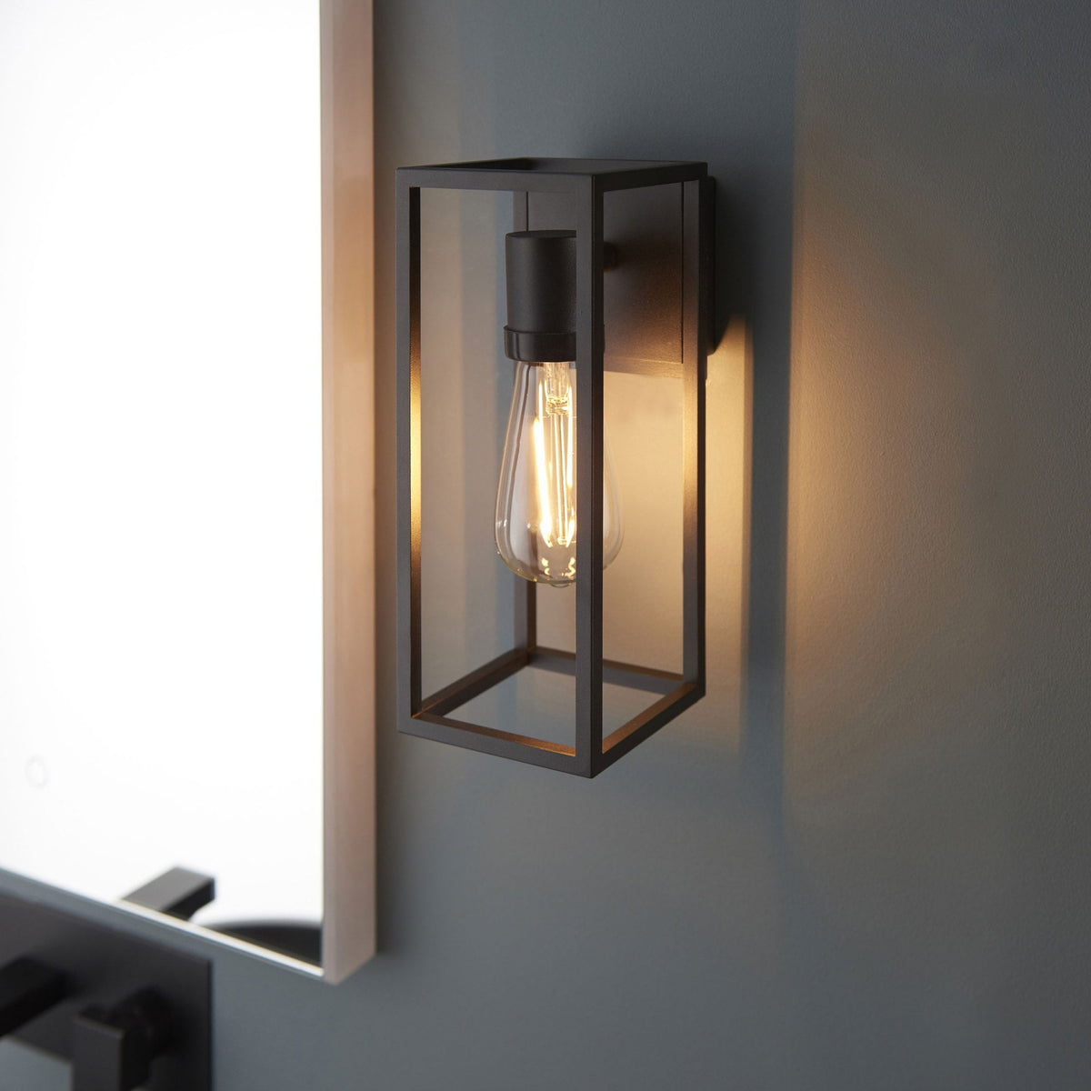 Close-up of a black framed wall light with an exposed filament bulb next to a mirror.