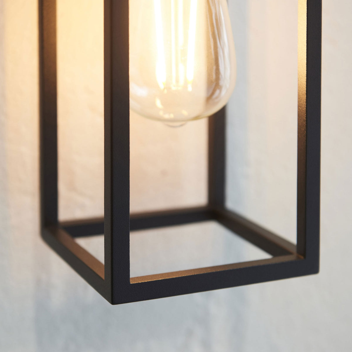 Close-up of the bottom of a black framed wall light, showing the exposed bulb and metal frame.