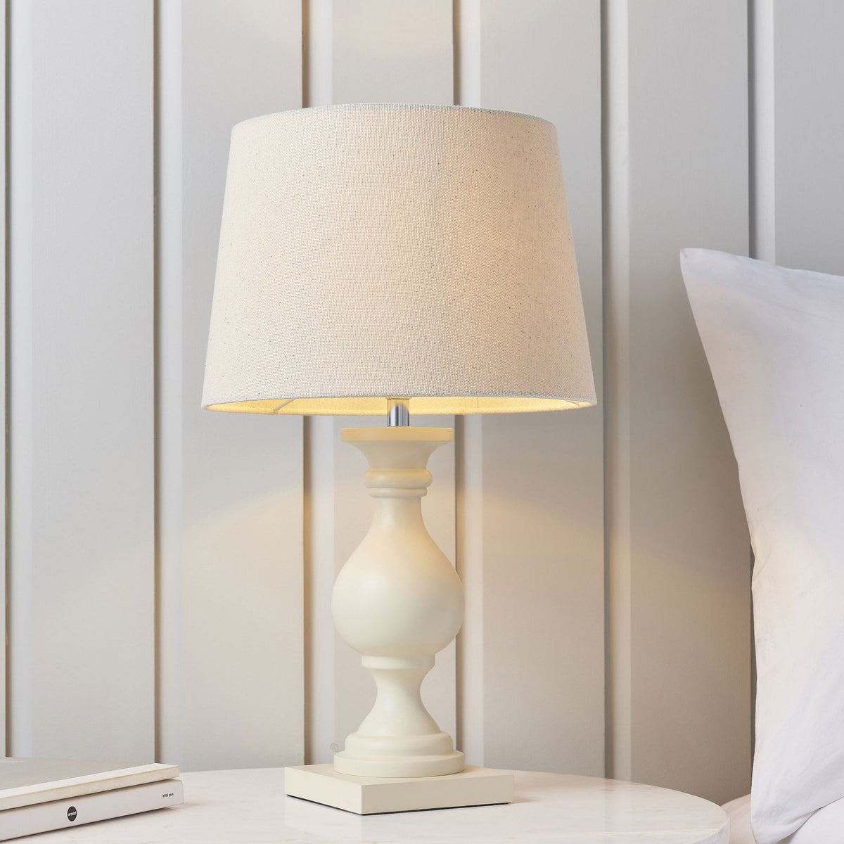 Cream table lamp with a linen shade on a white bedside table.