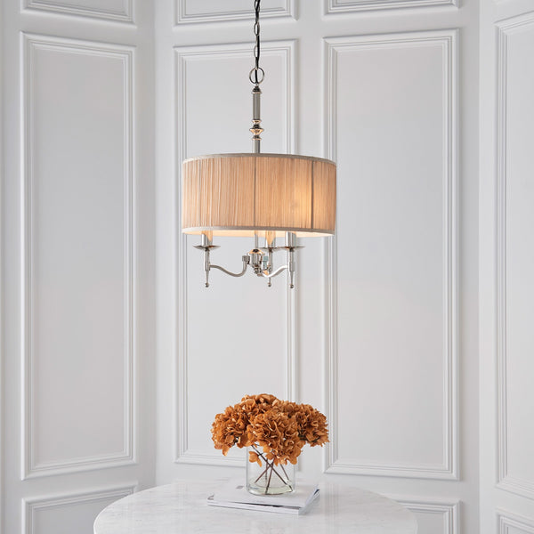 A beige chandelier hangs above a white table with a vase of dried flowers.