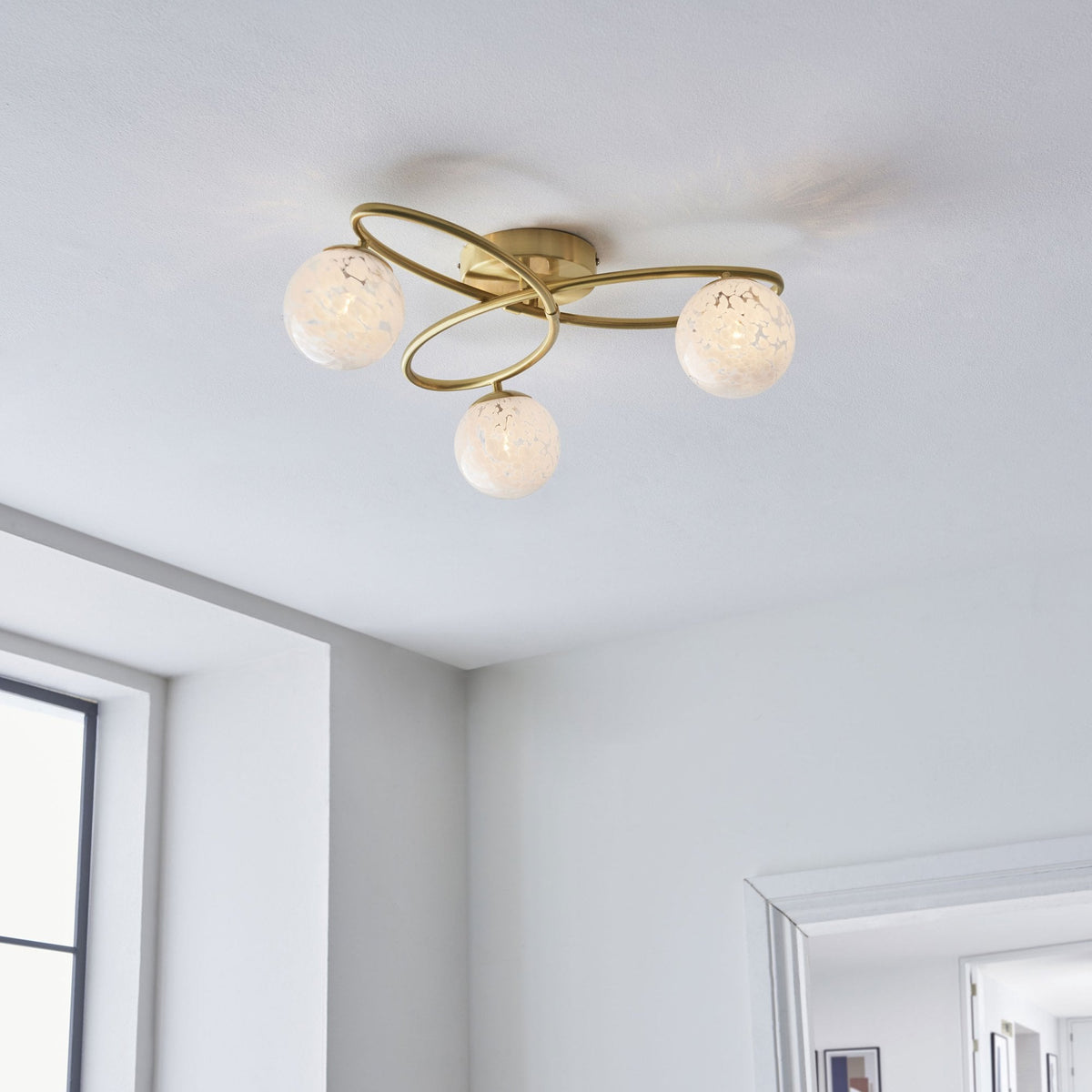 Three-light ceiling fixture with a brass frame and frosted glass globes in a bright room.