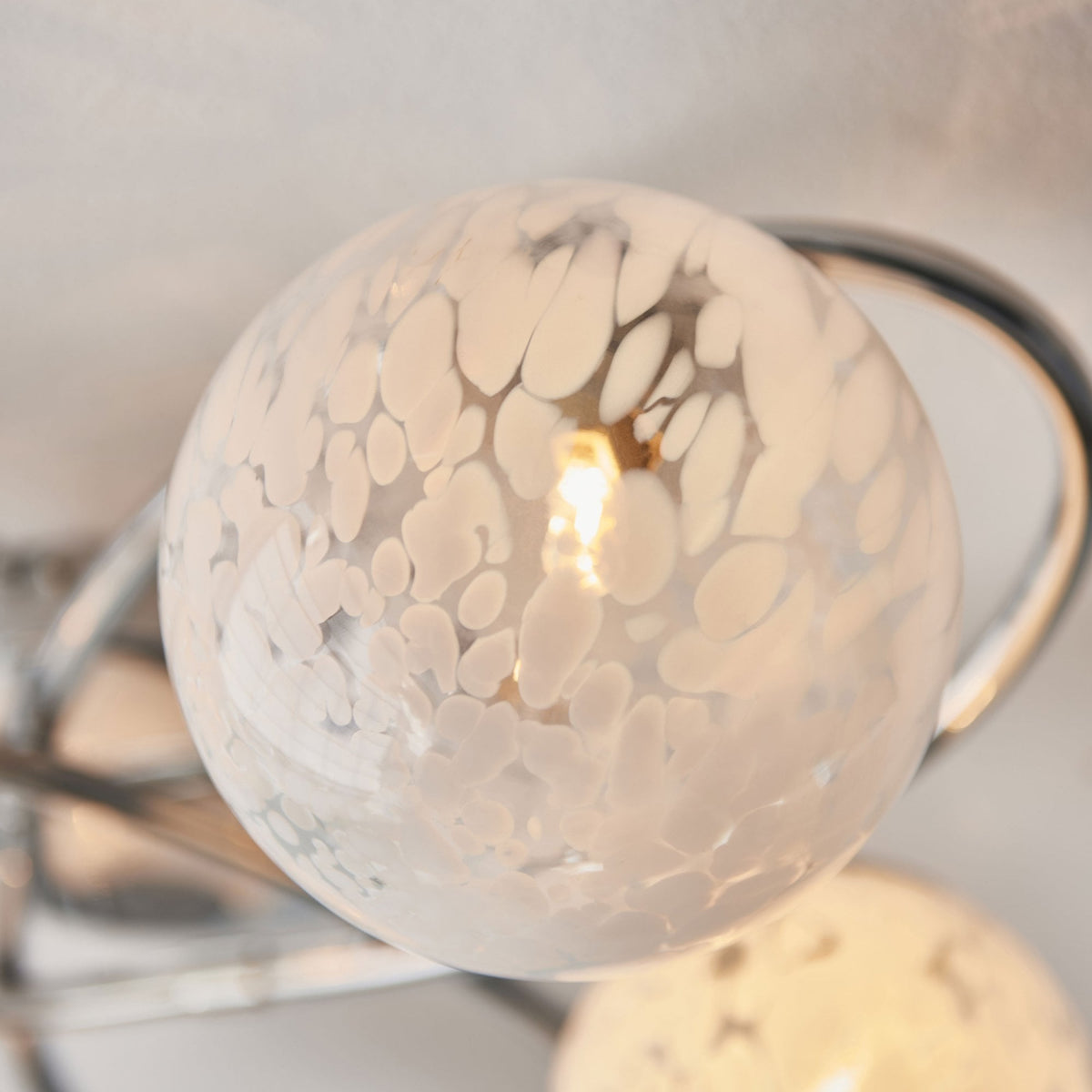 Close-up of a white speckled glass shade on a chrome ceiling fitting.